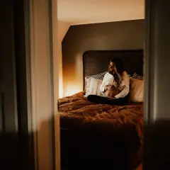 En kvinna med gravidmage sitter på en säng, omgiven av kuddar. Vackra gravidbilder hemma som fångar ögonblicket.