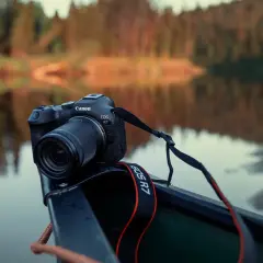 Canon EOS R7 redo i en kanot vid en spegelblank sjö med skog i bakgrunden.
