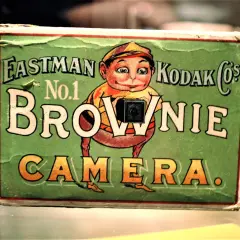 En grön låda med en tecknad figur som håller en kamera. Texten "Eastman Kodak Co.'s No.1 Brownie Camera" syns tydligt.
