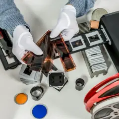 Händer med vita handskar sorterar diabilder och filmremsor för att skanna diabilder med mobilen. En filmrulle och färgfilter ligger bredvid.