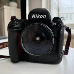 En svart Nikon F5 systemkamera med ett stort objektiv. Kameraremmen med texten "Nikon" syns.