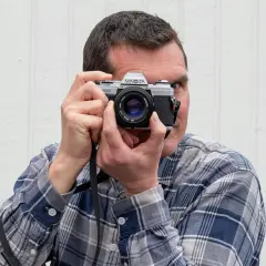 Man med rutig skjorta håller upp en Minolta-kamera för att fota analogt.