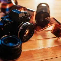 En svart analog kamera med filmrullar och objektiv på ett träbord. Detta ger en känsla av vad som menas med analogt.