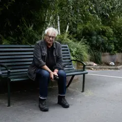 Anders Petersen sitter på en parkbänk, omgiven av grönska.