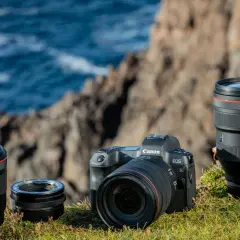 Canon R-serie kamerahus och objektiv, inklusive 50mm och 28-70mm, placerade på en gräsbevuxen klippa vid havet.