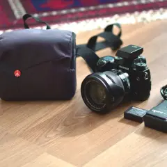 En Fujifilm XH1-kamera med objektiv, batteri, laddare och väska ligger på ett trägolv.