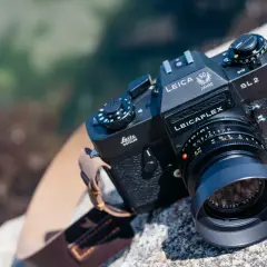 En svart Leicaflex SL2-kamera med ett objektiv och en läderrem ligger på en sten vid vattnet.