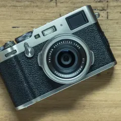 En Fujifilm X100T-kamera ligger på en träyta. Dess retrodesign och fasta objektiv gör den till en favorit för gatufotografering.