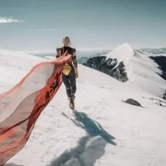 En kvinna med röd sjal vandrar på ett snötäckt berg. Emma Svensson fotograf.