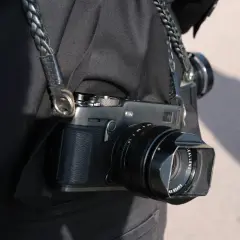 En person bär en svart jacka med en flätad läderrem som håller en Fuji Xpro 3-kamera.