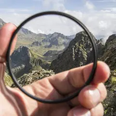 En hand håller upp ett filter framför en bergig dalgång.