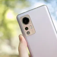 En hand håller en ljuslila Xiaomi 12 för ett test. Kameramodulen med 50MP syns tydligt mot en suddig grön bakgrund.