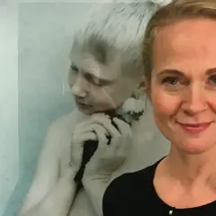 Anna Claren ler mot kameran, med en konstnärlig bild av en pojke som håller en fågel i bakgrunden.
