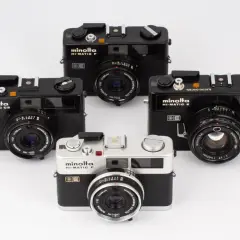 Fyra Minolta Hi-Matic kameror, varav en silverfärgad Minolta Hi-Matic F i förgrunden, omgivna av svarta modeller.