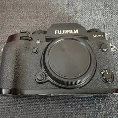 En svart Fujifilm X-T1 kamera ligger på en grå bakgrund.