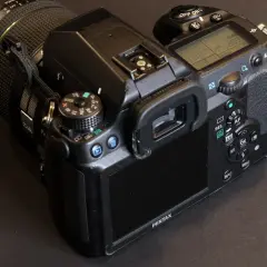 En närbild på en Pentax K5 systemkamera med objektivet på. Knappar och skärm syns tydligt.