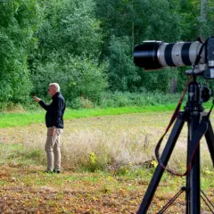 Man pekar i skogen. En kamera på stativ är redo för bildanalys.
