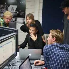 Studenter på **Nordens Fotoskola** diskuterar projekt framför datorskärmar.