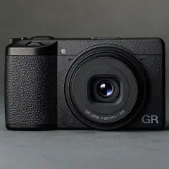 Svart kompaktkamera, en Ricoh GR III X, med texten "GR LENS f=26.1mm 1:2.8" på objektivet.