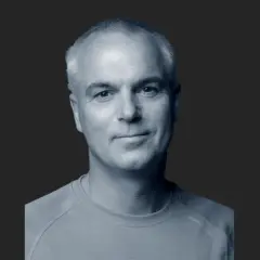 Porträtt av Paul Hansen, en man med grånande hår och ett vänligt leende, klädd i en ljusblå tröja.