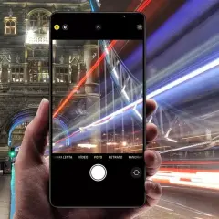 En hand håller en iPhone som fångar ljusspår från bilar vid Tower Bridge. En lång slutartid på iPhone ger en dramatisk effekt.