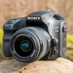 Sony a68 systemkamera med objektiv, placerad på en trädstam utomhus.