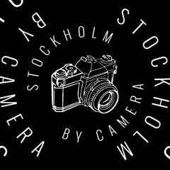 En vit ritad kamera omgiven av texten "STOCKHOLM CAMERA BY CAMERA" i en cirkel. Perfekt för stockholm fotomaraton.