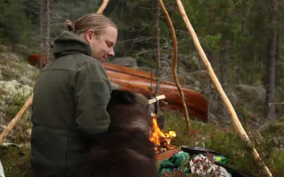 En man med en hund sitter vid en lägereld i skogen. En kanot ligger i bakgrunden. Detta är vad en fotosession betyder för dem.