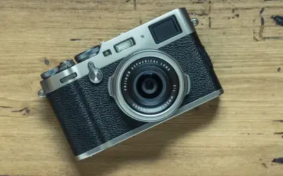 En Fujifilm X100T-kamera ligger på en träyta. Dess retrodesign och fasta objektiv gör den till en favorit för gatufotografering.