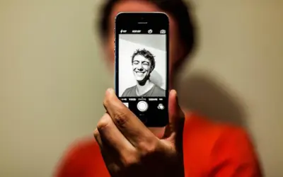 En person tar en selfie med en iPhone. Personen ler brett mot kameran.