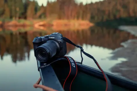 Canon EOS R7 redo i en kanot vid en spegelblank sjö med skog i bakgrunden.