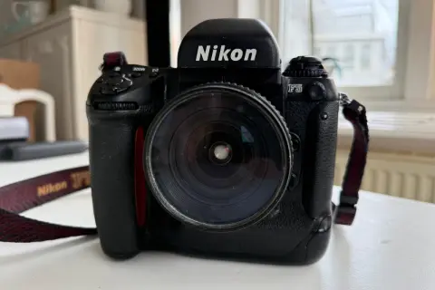 En svart Nikon F5 systemkamera med ett stort objektiv. Kameraremmen med texten "Nikon" syns.