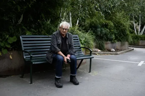Anders Petersen sitter på en parkbänk, omgiven av grönska.