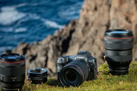 Canon R-serie kamerahus och objektiv, inklusive 50mm och 28-70mm, placerade på en gräsbevuxen klippa vid havet.