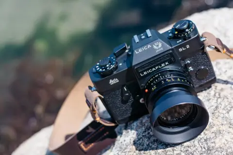 En svart Leicaflex SL2-kamera med ett objektiv och en läderrem ligger på en sten vid vattnet.
