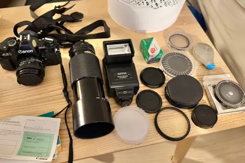 En Canon AE-1 kamera med objektiv, blixt, film och tillbehör ligger på ett träbord.
