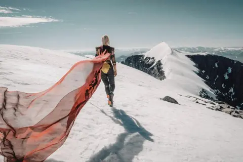 En kvinna med röd sjal vandrar på ett snötäckt berg. Emma Svensson fotograf.