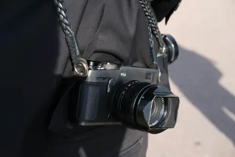 En person bär en svart jacka med en flätad läderrem som håller en Fuji Xpro 3-kamera.