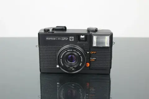 Svart Konica C35 EFP-kamera med blixt och Konica Hexanon-objektiv. Perfekt för att fånga klassiska ögonblick.
