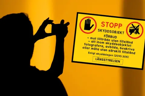 Silhuett av person som fotograferar. Gul skylt med texten "STOPP SKYDDSOBJEKT FÖRBUD" och symboler som varnar för att fotografera, avbilda eller mäta utan tillstånd.