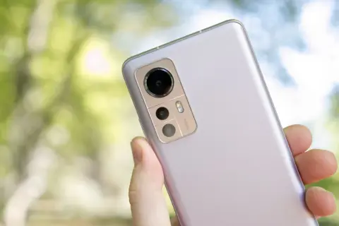 En hand håller en ljuslila Xiaomi 12 för ett test. Kameramodulen med 50MP syns tydligt mot en suddig grön bakgrund.