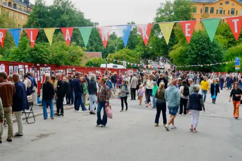 Färgglada vimplar med texten "Planket Stockholm" hänger över en livlig utomhusutställning med många besökare.