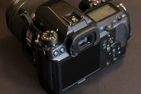 En närbild på en Pentax K5 systemkamera med objektivet på. Knappar och skärm syns tydligt.