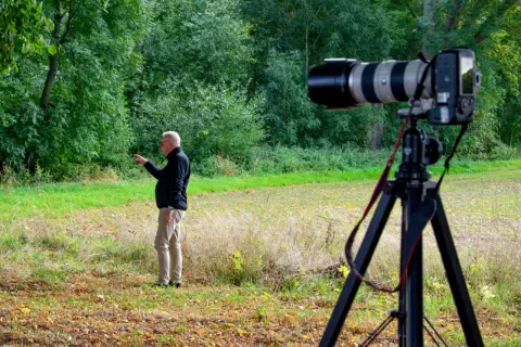 Man pekar i skogen. En kamera på stativ är redo för bildanalys.