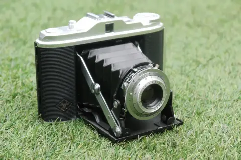 En klassisk Agfa Isolette hopfällbar kamera med läderdetaljer och en silverfärgad lins, placerad på grönt gräs.