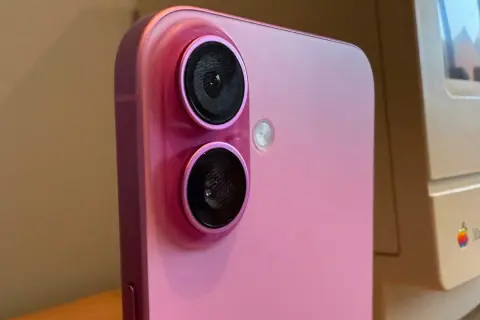 Rosa iPhone med dubbla linser på kameran, bredvid en gammal Macintosh-dator.