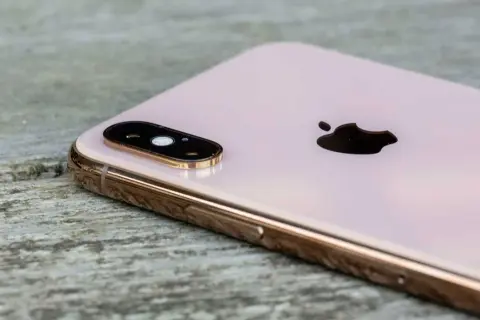 En rosa iPhone XS med dubbla linser på kameran, placerad på en träyta.