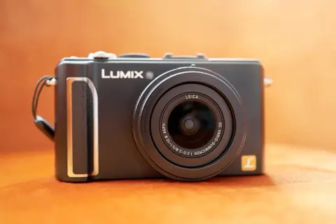 Svart kompaktkamera, en Lumix LX3 med Leica-objektiv, ligger på en orange yta.