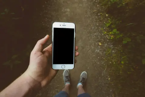 En hand håller en iPhone för att skanna bilder på en skogsstig.