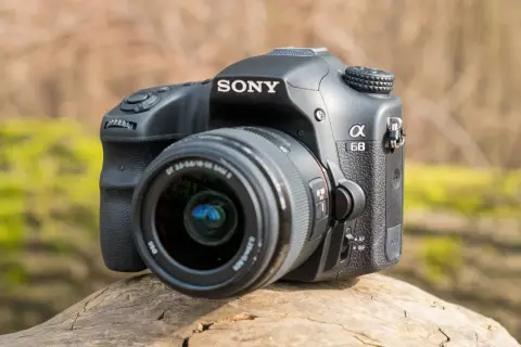 Sony a68 systemkamera med objektiv, placerad på en trädstam utomhus.